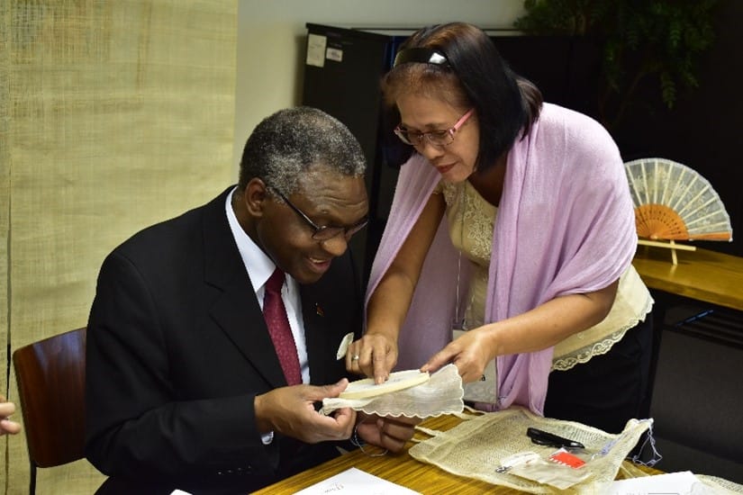 Photograph of a woman showing a man a piece of embroidery. 
