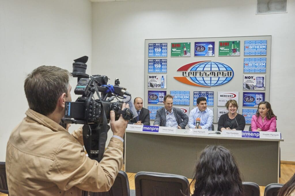 A man with a video camera films a table of five people sitting for an interview panel.