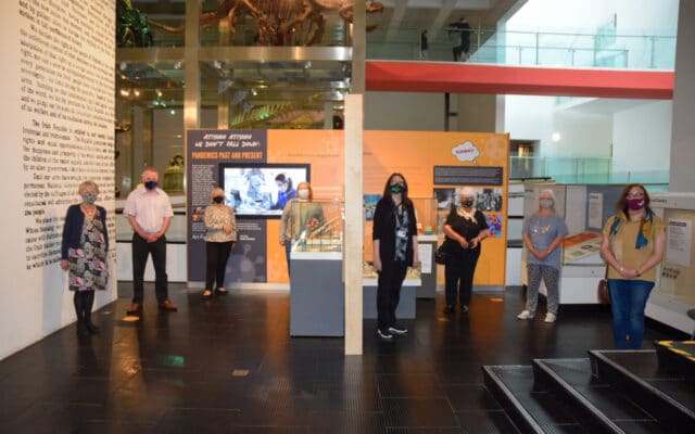 A group of people stand socially distanced wearing face masks in an exhibition space