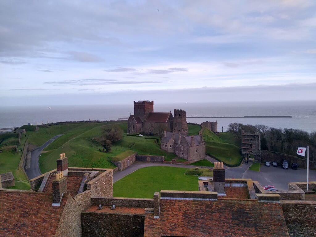 View from the top of Dover Castle looking at Roman Lighthouse and Church, with the sea in the background.