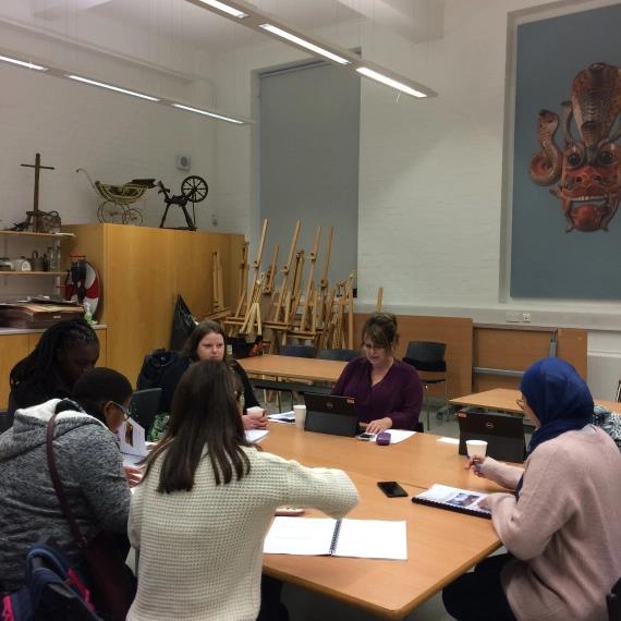Five women sit around a table with laptops, notebooks and pieces of paper