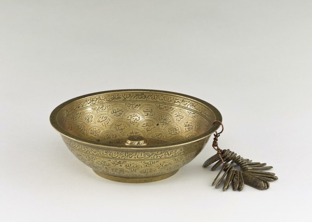 Brass bowl from India engraved with Arabic inscriptions and with engraved brass tags attached.