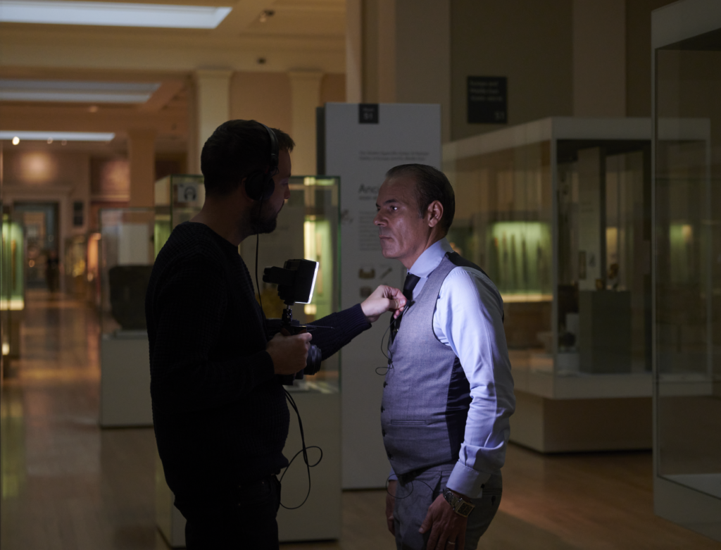 Lotfi being assisted with putting on a lapel microphone by cameraman.