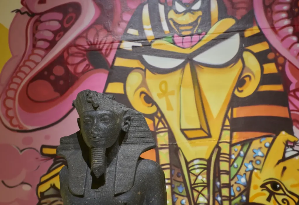 Close up of Tutankhamun reimagined display, with ancient statue of Tutankhamun placed in front of contemporary graffiti of Tutankhamun in the background.