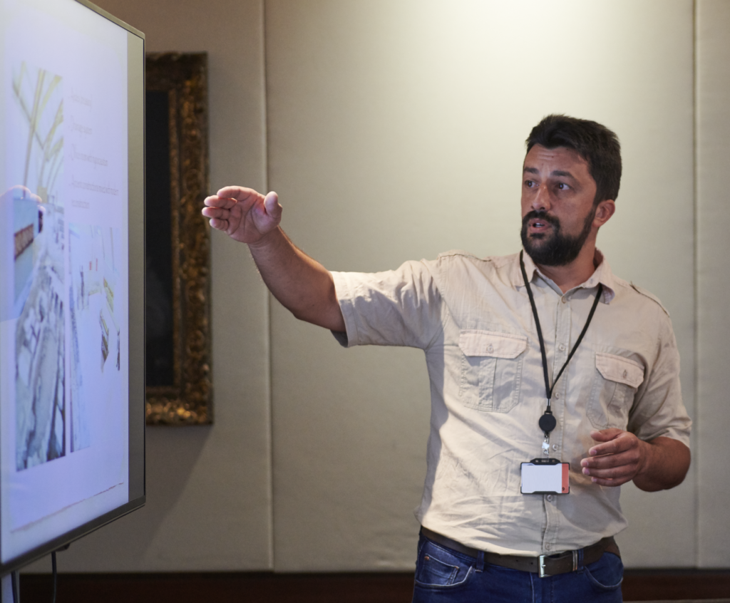 Ciprian standing up and pointing towards a television screen, giving a presentation.