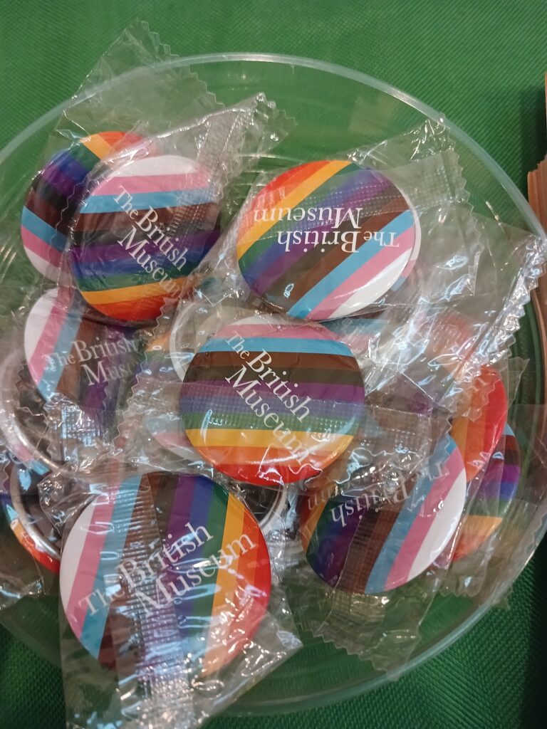 A bowl of badges with the British Museum logo in front of the rainbow pride colours.