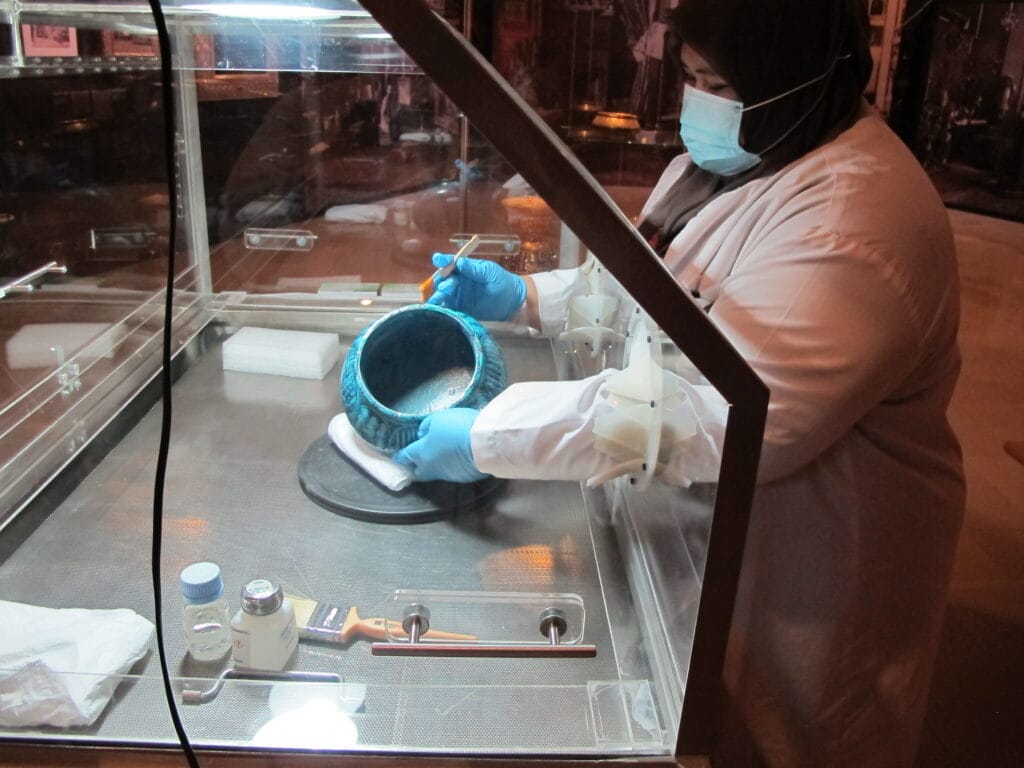 Rafidah cleaning an object in a display case.