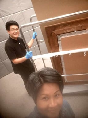 A selfie taken by Aprille with a man behind her wheeling objects on a trolley.