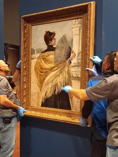 Photograph of a painting being held by three people.