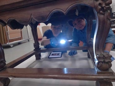 Two people inspecting a wooden table with a torch.