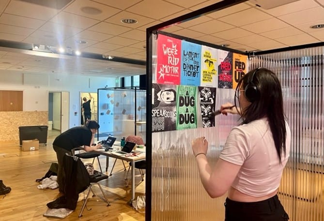 Photograph of a students hanging their work on display frames.