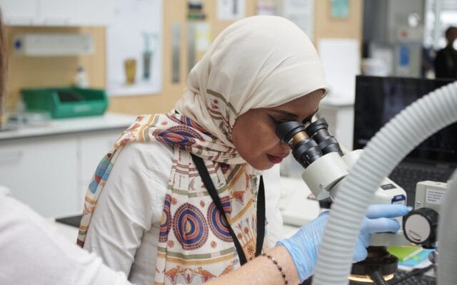 Photograph of a woman looking into a microscope.