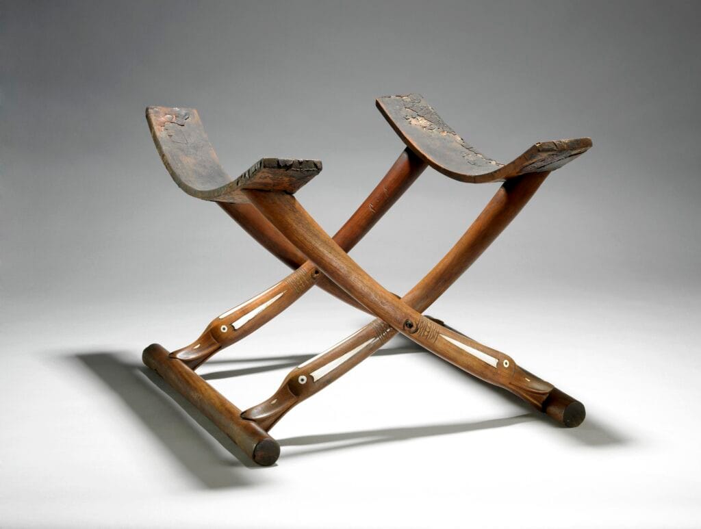 Wooden folding-stool. The well cut and finished base rails are cylindrical and without further decoration. The folding legs each terminate in a head of a duck or goose.